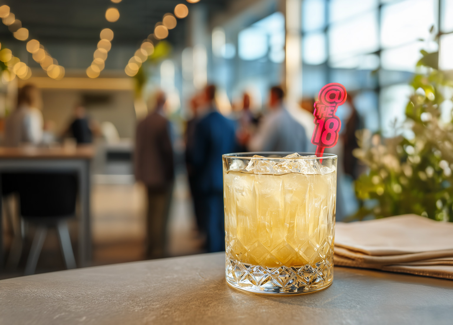 Branded Drink Stirrers for Corporate Events_Experiential Branding Guide. Custom Logo Stirrer in a rocks glass with Corporate Reception in the background.
